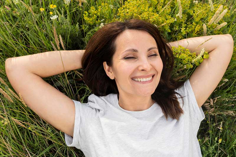 Frau liegt in Wiese mit Heilpflanzen und lächelt