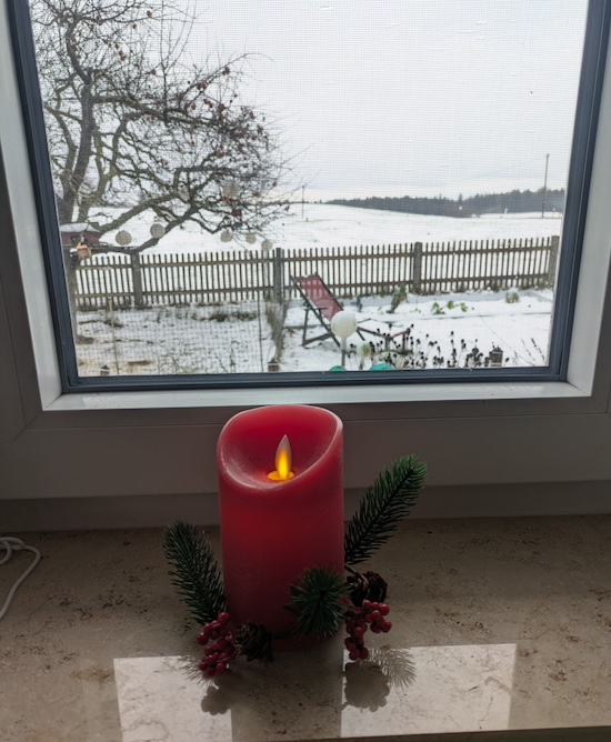 weihnachtsmitteilung2025 Weihnachtskerze auf Tannengrün am Fenster. Draußen verschneite Landschaft
